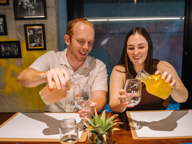 Two smiling people pouring cocktails into glasses